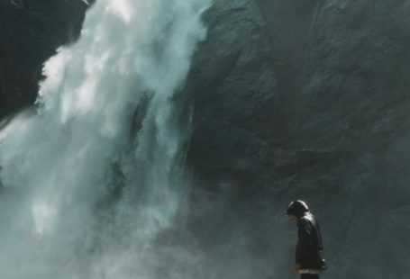 Waterfall Hikes - Man Standing on Brown Rock Cliff in Front of Waterfalls Photography