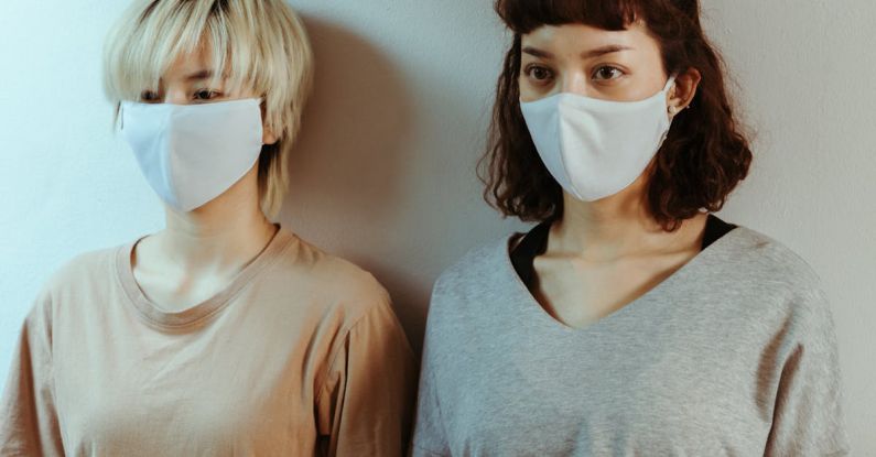 Benefits Of Staying - Asian women in home wear in medical masks attentively looking away while standing against white wall