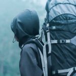 Backpacking - Man Wearing Black Hoodie Carries Black and Gray Backpacker Near Trees during Foggy Weather