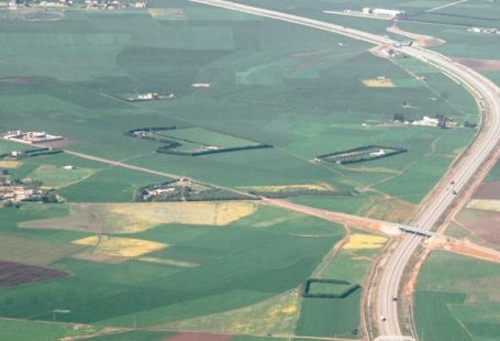 Vast Rural Areas - Aerial view of fields covered with green grass near asphalt serpentine road and cottage houses and farms