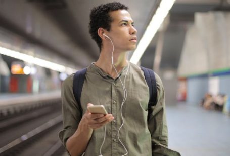 Underground Music - Young ethnic man in earbuds listening to music while waiting for transport at contemporary subway station